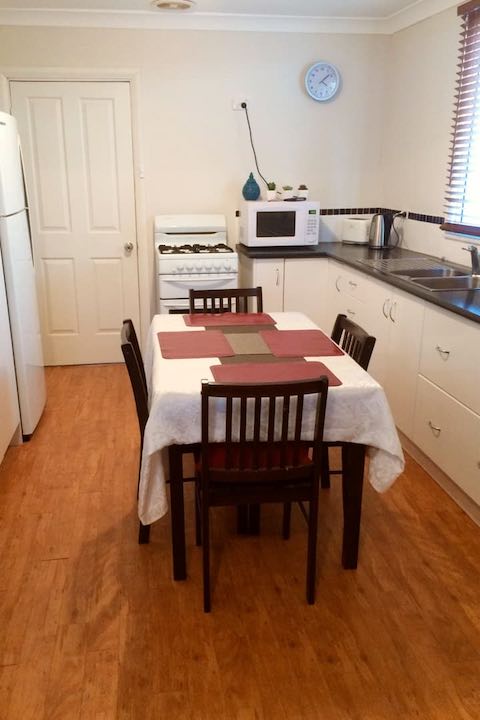 A kitchen, featuring a tall refrigerator, a gas cooker, a microwave, a kettle, and bench space.