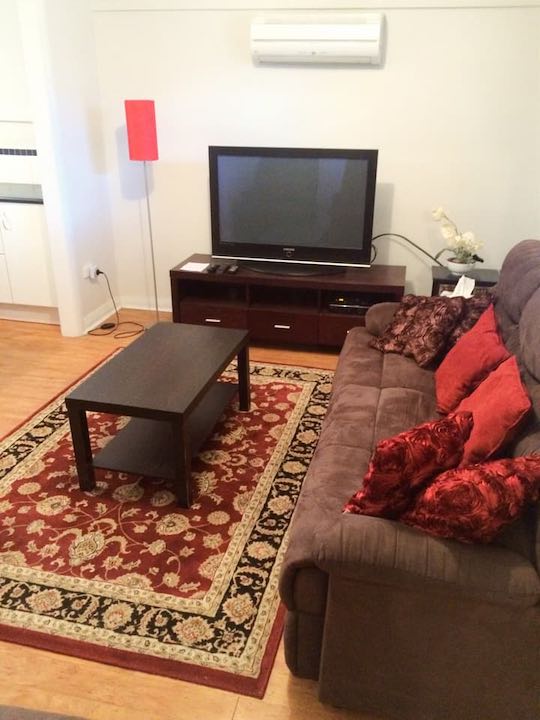 The living room, with a TV, comfortable lounge, and split system air conditioner.